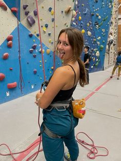 a woman climbing on a rock wall with ropes and harnesses around her waist, smiling at the camera