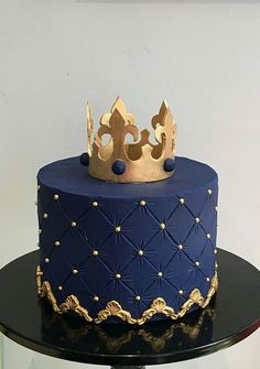 a blue and gold cake with a crown on top is sitting on a black table