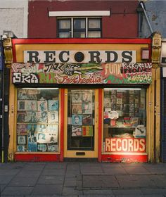 an old record store with many records on it's front window and windows covered in graffiti