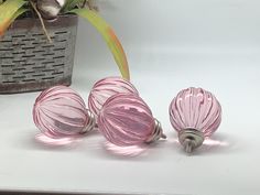 three pink glass knobs sitting on top of a white counter next to a potted plant