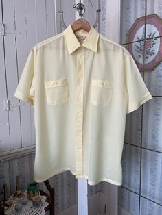 This is a very light weight, semi sheer dress shirt from Kingsport, made from 100 per cent polyester in pale buttery yellow (it's a bit darker than in the photos). The shirt has the original buttons on the front and two chest pockets with matching buttons. Marked size large. The measurements, taken with the shirt lying flat, are: shoulder to shoulder, 19 inches; armpit to armpit, 23 inches; sleeves, 10 1/2 inches; length, 31 inches; bottom edge, 26 inches. In very good condition. Light Yellow Button Up Shirt, Collared Cream Shirt For Summer, Classic Summer Shirt For Daywear, Solid Vintage Summer Shirt, Cream Collared Shirt For Summer, Summer Cream Collared Shirt, Solid Color Summer Shirt For Daywear, Yellow Short Sleeve Shirt For Summer, Summer Short Sleeve Shirt For Daywear