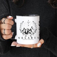 a woman holding a white coffee mug with the words velaris printed on it