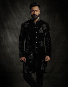 a man standing in front of a dark background wearing a black jacket and pants with flowers on it