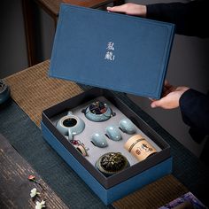 an open blue box containing various items on a table with two hands reaching for it