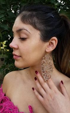 a woman in a pink dress is holding her hand up to her ear and wearing large gold earrings