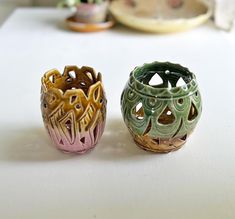 two small vases sitting on top of a white table next to each other in different colors