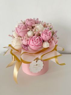 pink and white flowers in a pink box with gold ribbon around the top, on a white background