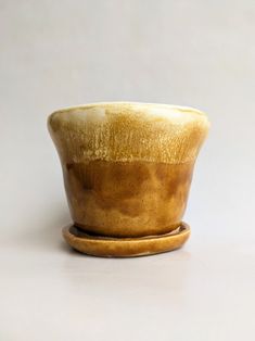 a brown and white bowl sitting on top of a wooden saucer next to a gray wall