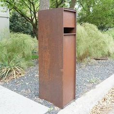 a rusted metal trash can sitting on the side of a road next to a tree