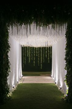 an outdoor wedding ceremony with white drapes and flowers hanging from the ceiling over the aisle