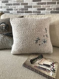 two knitted pillows sitting on top of a couch next to a book and sunglasses