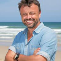 a man standing on the beach with his arms crossed and looking at the camera smiling