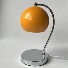 an orange table lamp on a silver base with a white light behind it and a grey background