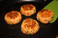 four crab cakes cooking in a pan with a green spatula next to them on the stove