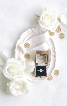 a ring with a diamond on it surrounded by white roses and gold coins in the background