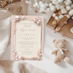 a teddy bear sitting next to a pink and white wedding card with pearls on it