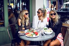 three beautiful women sitting at a table with plates of food