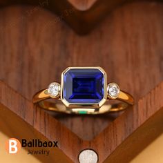 a gold ring with a blue stone and two diamonds on it, sitting on a wooden stand