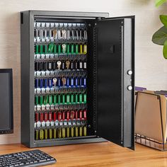 a computer monitor and keyboard sitting next to a metal cabinet filled with pens and scissors