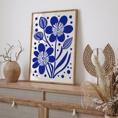 a blue and white flower art print on a shelf next to some dried plant life