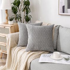 a living room with a couch, coffee cup and plant on the end table in front of it