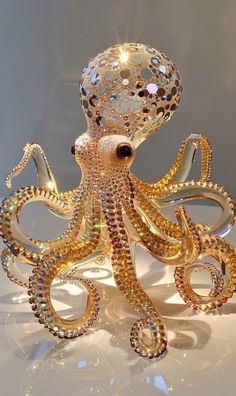 an octopus sculpture made out of gold and crystal beads on a white surface with sunlight shining through