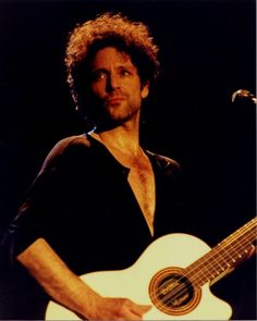 a man with curly hair holding a white guitar