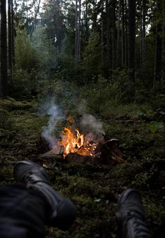 a person sitting in front of a campfire with their feet up on the ground