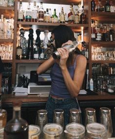 a woman standing behind a bar filled with bottles