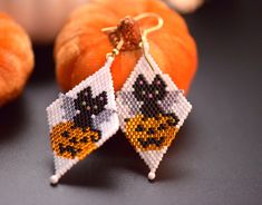 the beaded earrings are decorated with black and white cats on them, sitting next to pumpkins