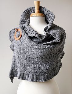 a white mannequin wearing a gray knitted shawl with a wooden ring on it