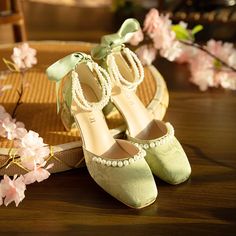 a pair of green shoes sitting on top of a wooden table next to pink flowers