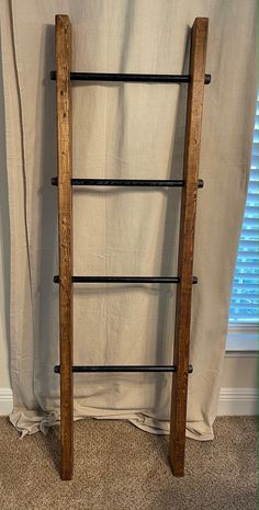 an old wooden ladder leaning against a wall in front of a window with white curtains