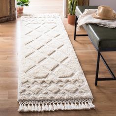 a long white rug with tassels on the floor next to a chair and potted plant