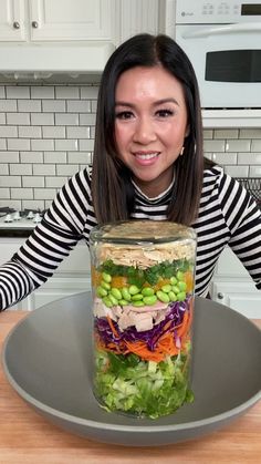 a woman sitting in front of a glass jar filled with vegetables