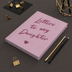 a pink notebook with the words letters to my daughter written on it next to some gold objects