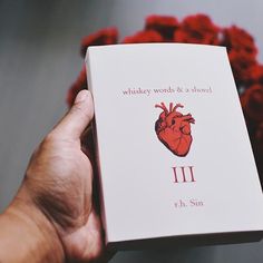 a person holding up a book with a heart on it and the title written in red