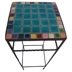 a small table with colorful tiles on it's top and metal frame, against a white background