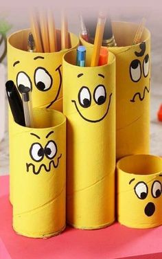 some pens and pencils are in yellow cups with faces drawn on the paper tubes