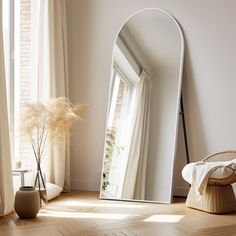 a large mirror sitting on top of a wooden floor next to a vase filled with flowers