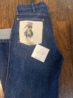 These are 13MWZ Original Indigo Mens Sizes ( add 2-3 sizes up from your actual size for the 13MWZ) This is a size (32 ) in  Mens .  WRANGLER "WILD WEST" Jeans are so fun & give that "WILD" edge to a pair of original Wranglers!!  "Wild West " Jeans are unique as each one adorns a Old West Vintage pic & the Savage Vaquera patch on every pair !!  Wear them casual, or dress them up for a night out on the town !!   "THE OUTLAW"-  adorns the left pocket, pocket has been stitched & is not accessible !   DO NOT MACHINE WASH ON HOT/ COLD CYCLE ONLY-  INSIDE OUT & HANG TO DRY  DO NOT PUT IN A HOT DRYER ** GO OVER WITH A WARM IRON IF NEEDED** Western Jeans Women, Western Thrift Finds, Out West Outfits, 80s Country Fashion, Diy Western Clothes, Western Concert Outfits Women, Vintage Western Outfits, Western Rodeo Outfits, Wrangler Fashion