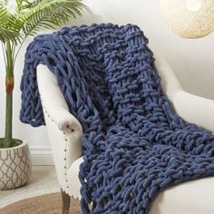 a blue knitted blanket sitting on top of a white chair next to a potted plant