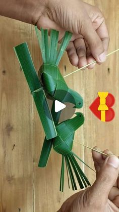 someone is making a paper mask out of green leaves and red stickers on a wooden table