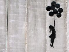 a person holding some black balloons in front of a wooden wall with a quote on it