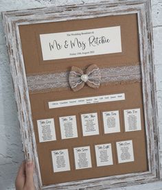 a hand holding up a framed wedding seating chart with a bow on the front and back