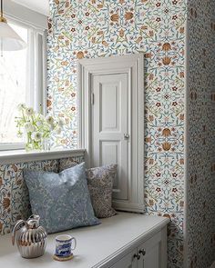 a window seat with pillows and a vase on it in front of a wallpapered room