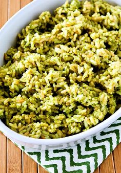 a white bowl filled with green rice on top of a wooden table