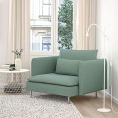 a green chair sitting in front of a window next to a white table with a lamp on it