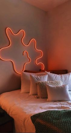 a bed with white sheets and pillows in front of a neon sign on the wall