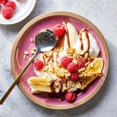 a pink plate topped with bananas, raspberries and yogurt covered in granola